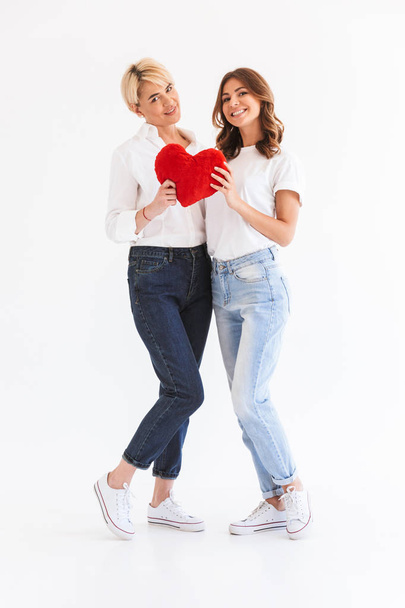 Image of beautiful young lady standing with her mother holding heart isolated over white background. - 写真・画像