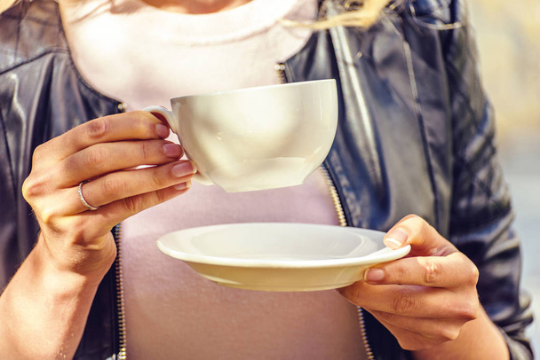 レザー ジャケット茶カップから飲むと料理を保持の女性。クローズ アップ撮影背景をぼかし。キシナウ、モルドバ - 写真・画像