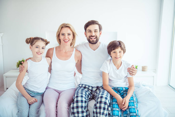 Young happy smiling family four persons sitting together on bed laughing hugging - Foto, Imagen