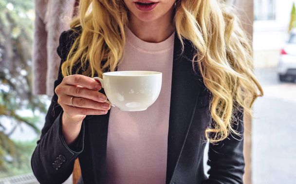 Vrouw het drinken van thee vanaf witte cup in restaurant in koude herfstdag. Close-up shot. Chisinau, Moldavië - Foto, afbeelding