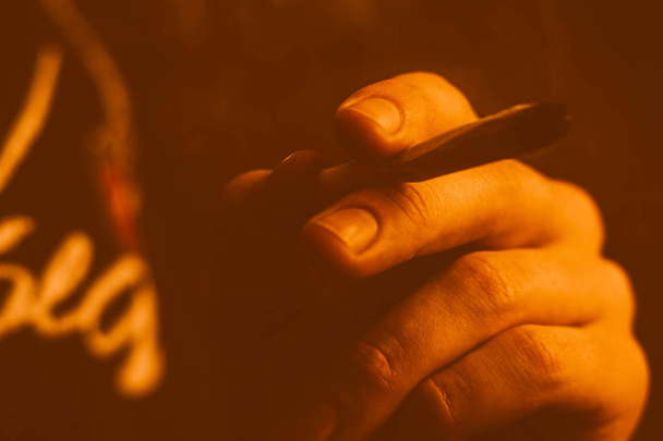 Een man rookt cannabis onkruid, een gezamenlijke en een aansteker in zijn handen. Gele toning - Foto, afbeelding