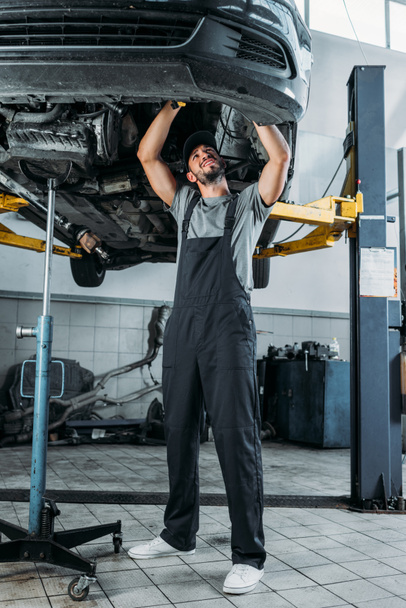 professional worker in uniform repairing a car in mechanic shop - Photo, image
