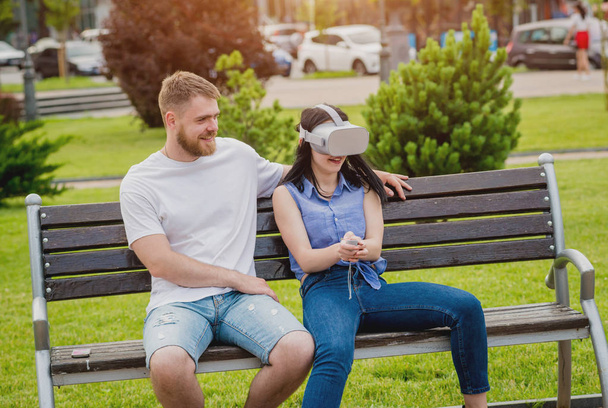 Young caucasian couple plays a game using virtual reality glasses on the street. VR headset. - Φωτογραφία, εικόνα