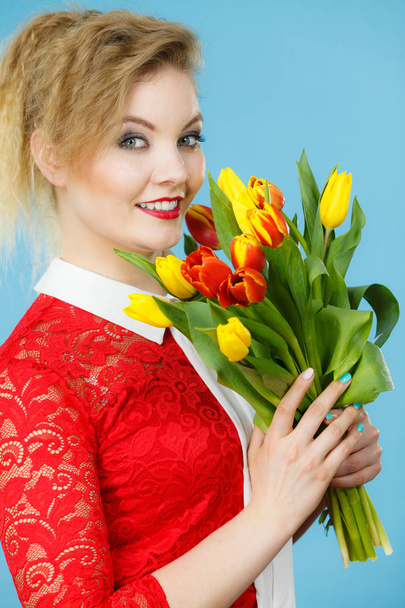 Día Internacional de la Mujer, ocho de marzo. Hermoso retrato de mujer bonita cabello rubio con tulipanes rojos amarillos, maquillaje de moda, traje elegante. Día de la madre. En azul
 - Foto, Imagen