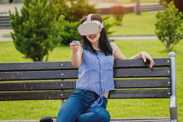 Attractive young girl plays a game wearing virtual reality glasses on the street. VR headset. - Foto, imagen