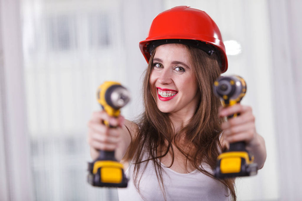 Young positive woman using power driil for work at home. Girl working at flat remodeling. Building, repair and renovation. - Foto, afbeelding