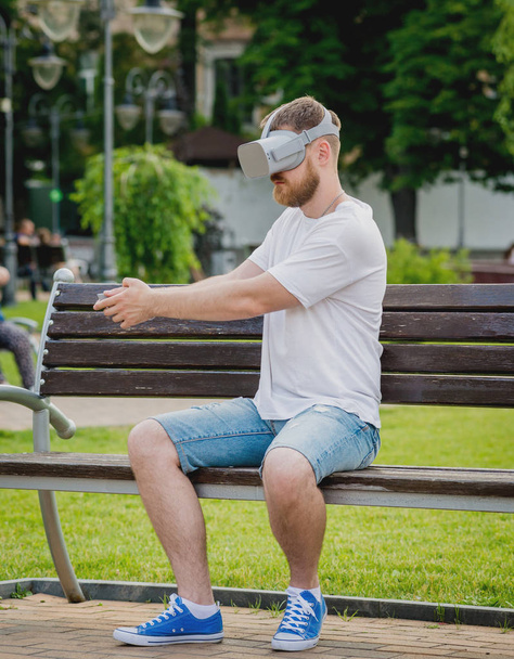 Young blond beardy man plays a game wearing virtual reality glasses on the street. VR headset. - Photo, Image