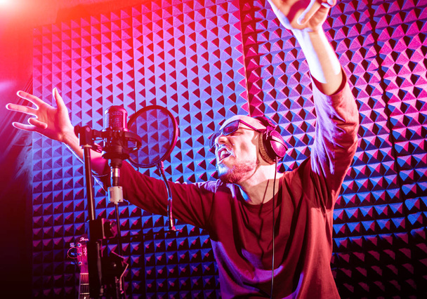 Ο τραγουδιστής τραγουδά με το μικρόφωνο στο στούντιο ηχογράφησης. Σύγχρονη φόντο - Φωτογραφία, εικόνα