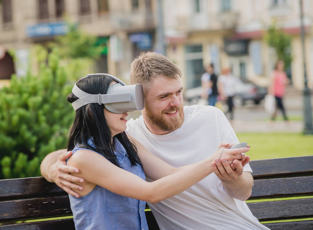Young caucasian couple plays a game using virtual reality glasses on the street. VR headset. - Foto, imagen