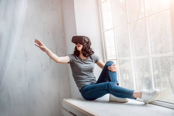 Young girl wearing virtual reality goggles sitting by the window - Foto, immagini