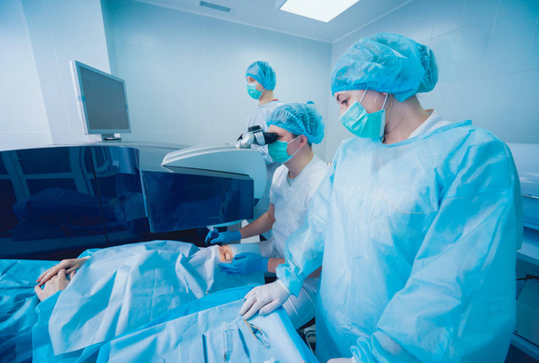 potilas ja kirurgit leikkaussalissa silmäleikkauksen aikana
 - Valokuva, kuva