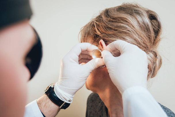 Otolaryngologist examines woman's ear with dilator. Medical equipment - Foto, imagen