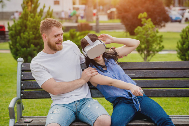 Young caucasian couple plays a game using virtual reality glasses on the street. VR headset. - Foto, Imagen