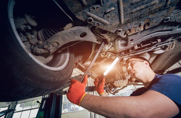 Car mechanic examining car suspension of lifted automobile at repair service station. Background - Foto, Bild