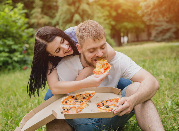 junges Paar beim Pizzaessen im Park. Sie behandeln einander und lachen. - Foto, Bild