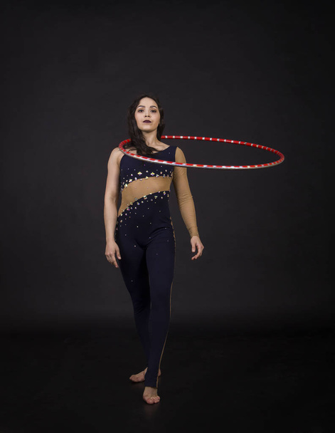 Gymnastic exercises with hula-Hoop girl performs circus performer in an artistic costume. Studio shooting on a dark background. - Фото, зображення