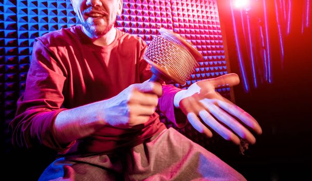 Young man playing on maracas in sound recording studio. Modern background - 写真・画像