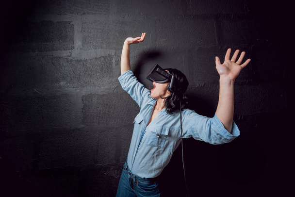 Young girl wearing virtual reality goggles before black wall - Valokuva, kuva