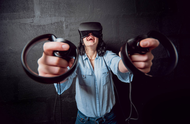 Young girl wearing virtual reality goggles before black wall - Foto, Imagem