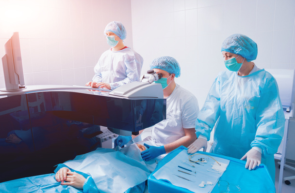 patient and team of surgeons in operating room during ophthalmic surgery - Фото, изображение