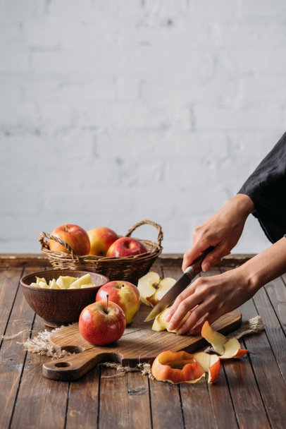 обрезанный снимок женщины, режущей яблоки на деревянной доске
 - Фото, изображение