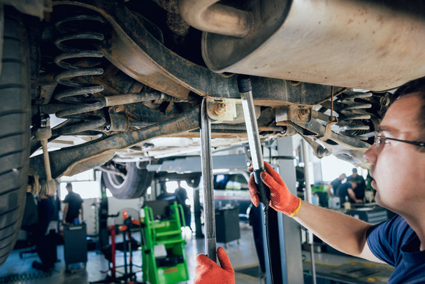Car mechanic examining car suspension of lifted automobile at repair service station. Background - Foto, Bild