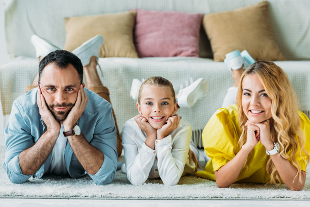 glückliche junge Familie liegt zu Hause auf dem Boden und blickt in die Kamera - Foto, Bild