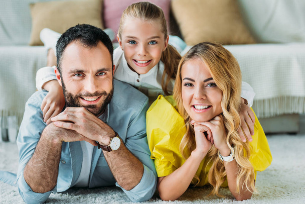 smiling young family lying on floor at home and looking at camera - Photo, Image