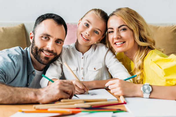 happy young family drawing with color pencils together and looking at camera - Photo, image