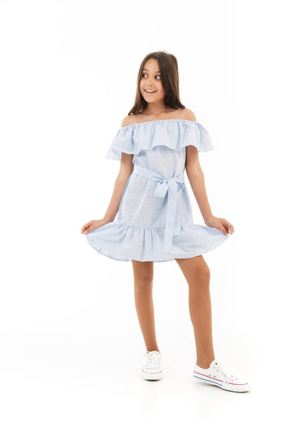 Full length image of Playful young brunette girl in dress posing and looking away over white background - Fotografie, Obrázek