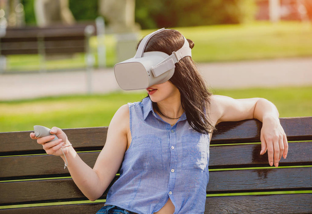 Houkutteleva nuori tyttö pelaa peliä yllään virtuaalitodellisuus lasit kadulla. VR kuulokkeet
. - Valokuva, kuva