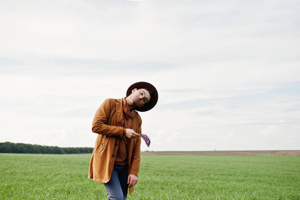 Stylish man in glasses, brown jacket and hat posed on green field. - Valokuva, kuva