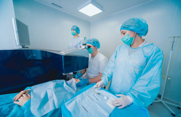 patient and team of surgeons in operating room during ophthalmic surgery - Foto, Imagen
