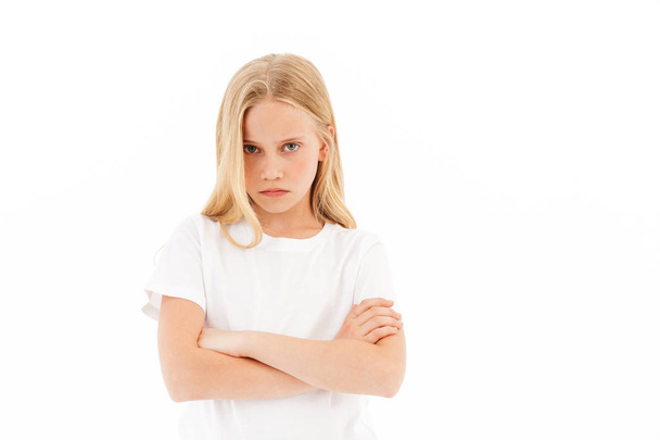 Offended young blonde girl in casual clothes posing with crossed arms while looking at the camera over white background - Fotografie, Obrázek
