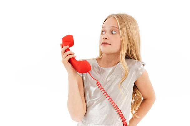 Picture of Scared surprised young blonde girl in dress talking by telephone over white background - Zdjęcie, obraz