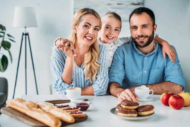 heureux jeune famille avec petit déjeuner sur la table en regardant la caméra
 - Photo, image