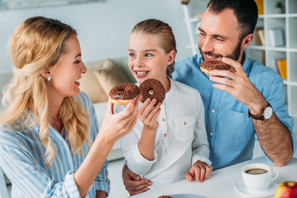 Szczęśliwa młoda rodzina jedzenie czekolady przeszklone pączki - Zdjęcie, obraz