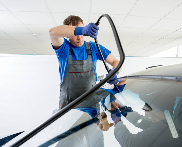 Automobile special workers replacing windscreen of car in auto service station garage - 写真・画像