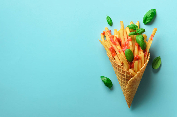 Fried potatoes in waffle cones on blue background. Hot salty french fries with tomato sauce, basil leaves. Fast food, junk food, diet concept. Top view. Minimal style. Pop art design, creative concept - Foto, Bild