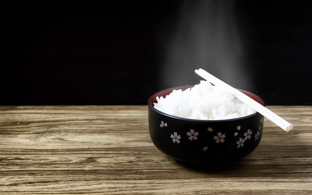 Ahşap zemin üzerinde siyah bir kasede pirinç sıcak yemek çubukları - Fotoğraf, Görsel