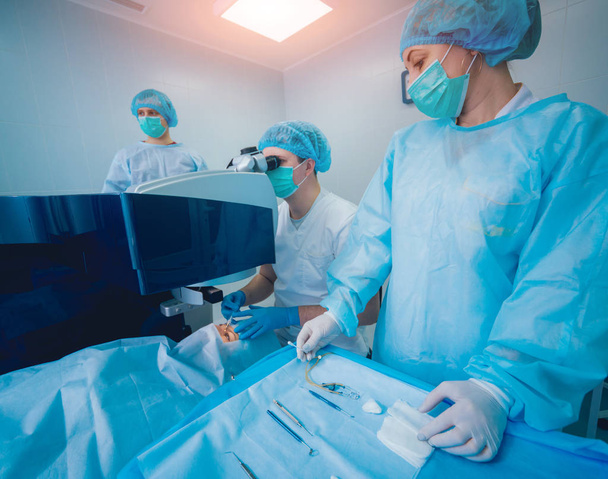 patient and team of surgeons in operating room during ophthalmic surgery - Photo, Image