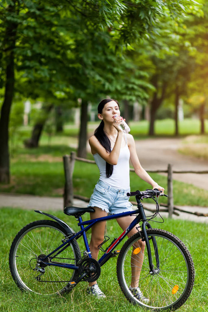 Bisiklet Şehir Parkı içme suyunda rahatlatıcı güzel kızla. Aktif insanlar. Açık havada - Fotoğraf, Görsel