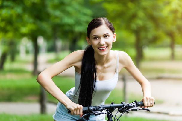 Mooi meisje een fiets in een stadspark. Actieve mensen. Buitenshuis - Foto, afbeelding