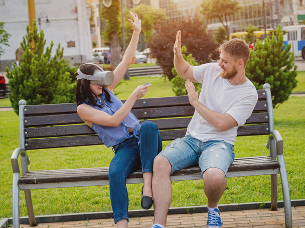 Young caucasian couple plays a game using virtual reality glasses on the street. VR headset. - Foto, Imagem