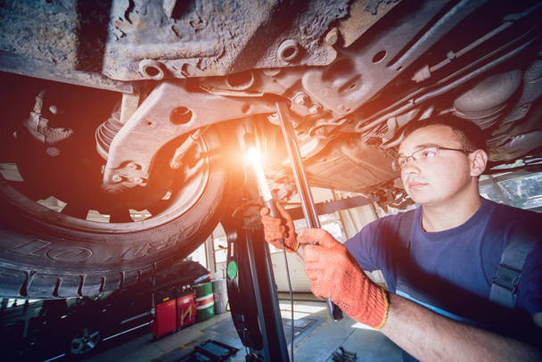 Kfz-Mechaniker bei der Untersuchung der Fahrwerksaufhängung des angehobenen Fahrzeugs an einer Reparaturstation. Hintergrund - Foto, Bild