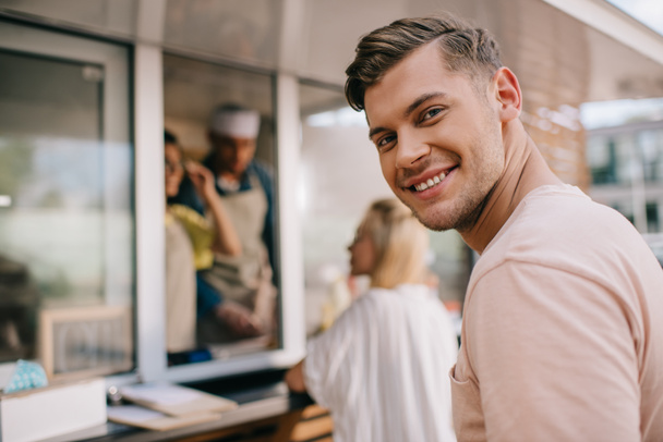 handsome young man smiling at camera while standing in line at food truck - Foto, imagen