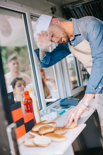 tired chef working in food truck while customers waiting outside - Photo, Image