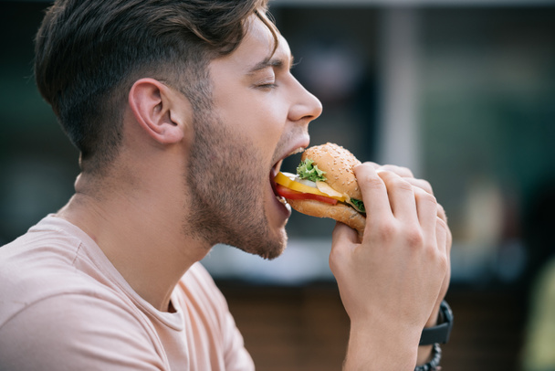 side view of man eating tasty burger with closed eyes - Photo, Image
