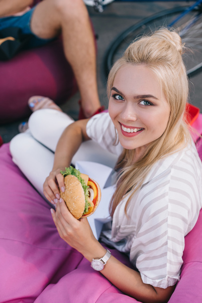 hoge hoekmening van aantrekkelijke vrouw houden hamburger en camera te kijken - Foto, afbeelding