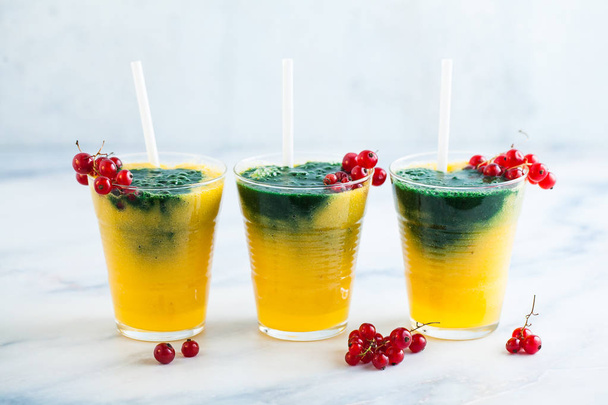 two colored fresh smoothies in glasses with fresh berries. orange banana juice with spirulina powder. detox breakfast. healthy eating - Photo, image